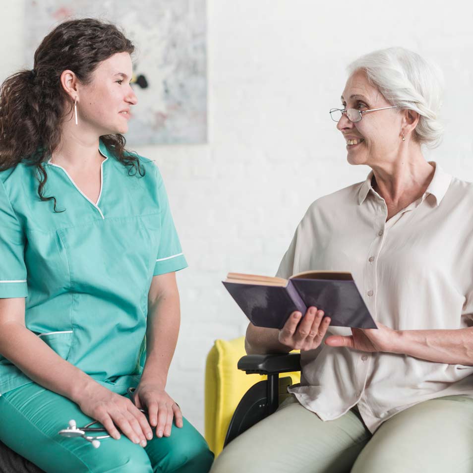 attractive nurse looking senior woman patient sitting wheel chair with book
