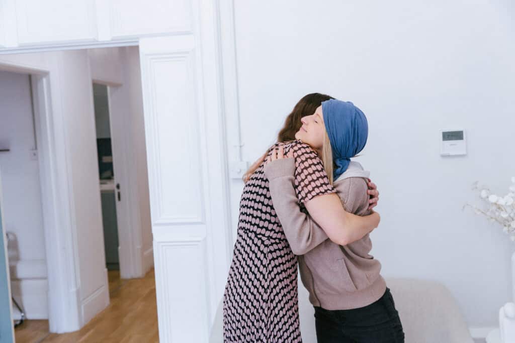Two women sharing a warm hug in a bright room, one wearing a blue headscarf